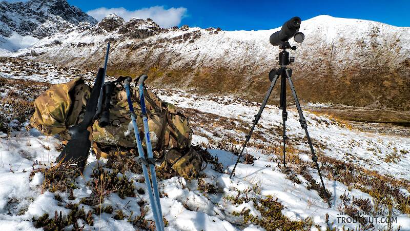 Mountain hunting gear. A rifle, spotting scope, and trekking poles rest with a backpack high in the Alaskan mountains